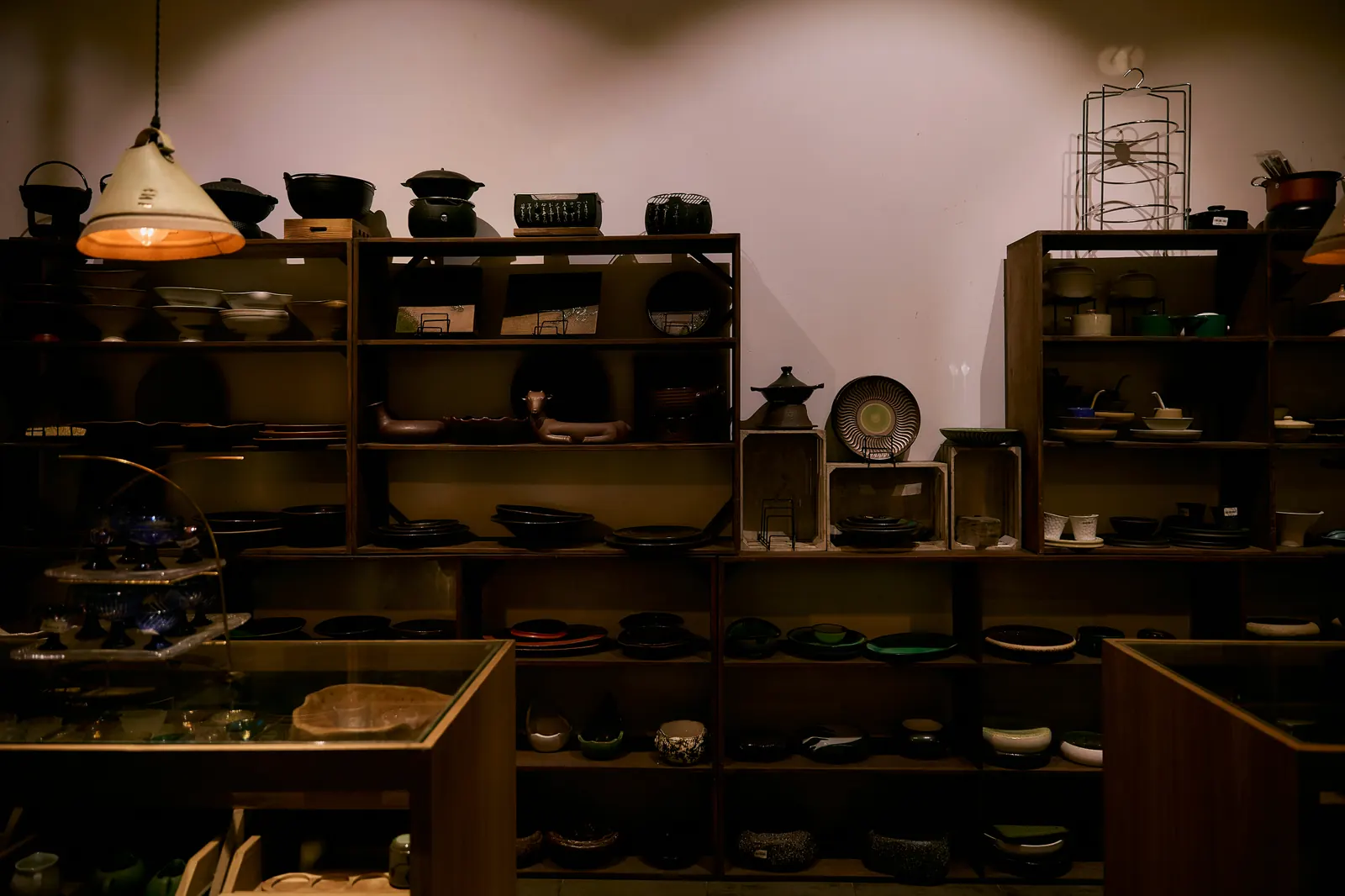 Ceramic dishes, bowls and lidded pots on warmly lit wooden display shelves