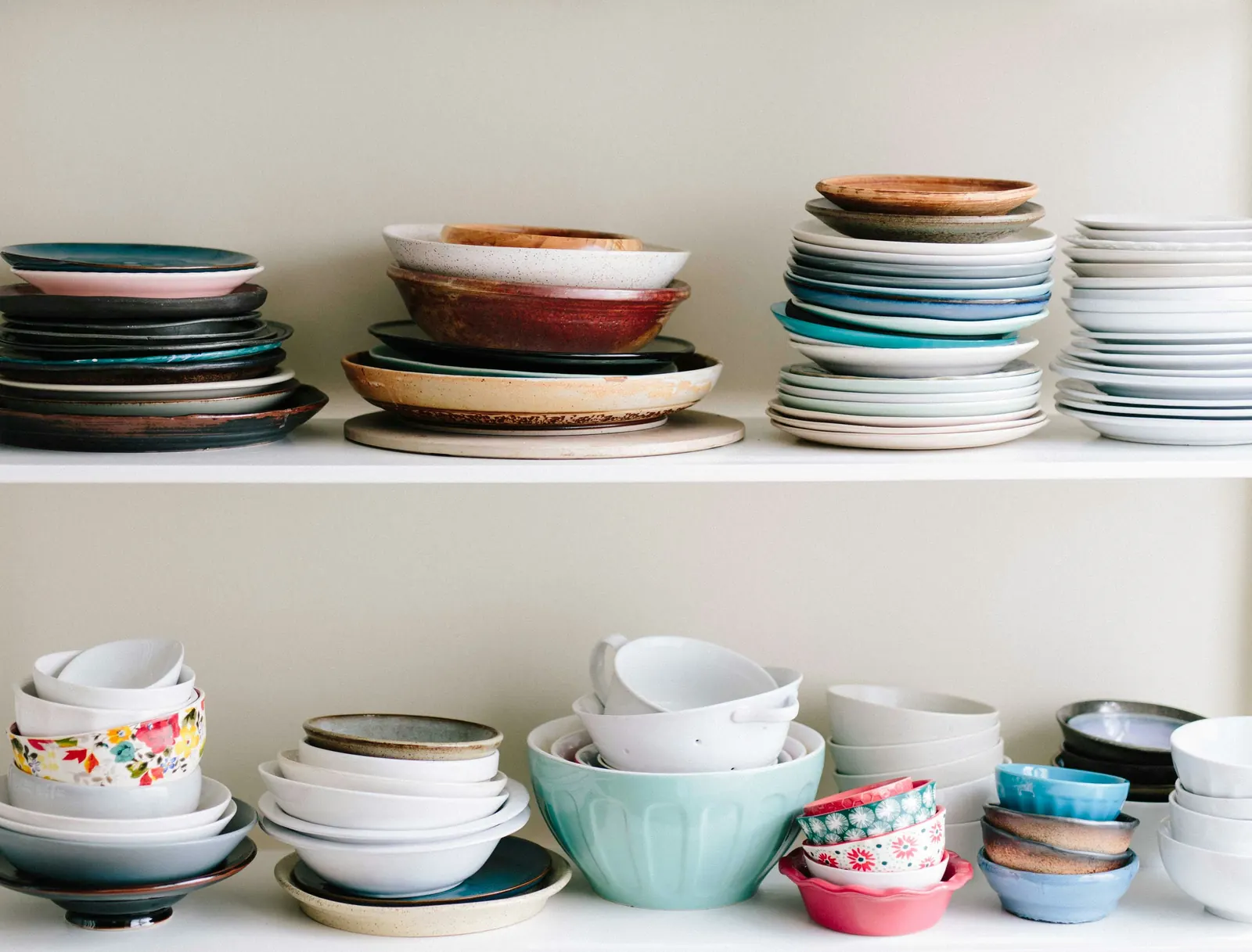 Stacks of glazed ceramic plates and bowls on white shelves