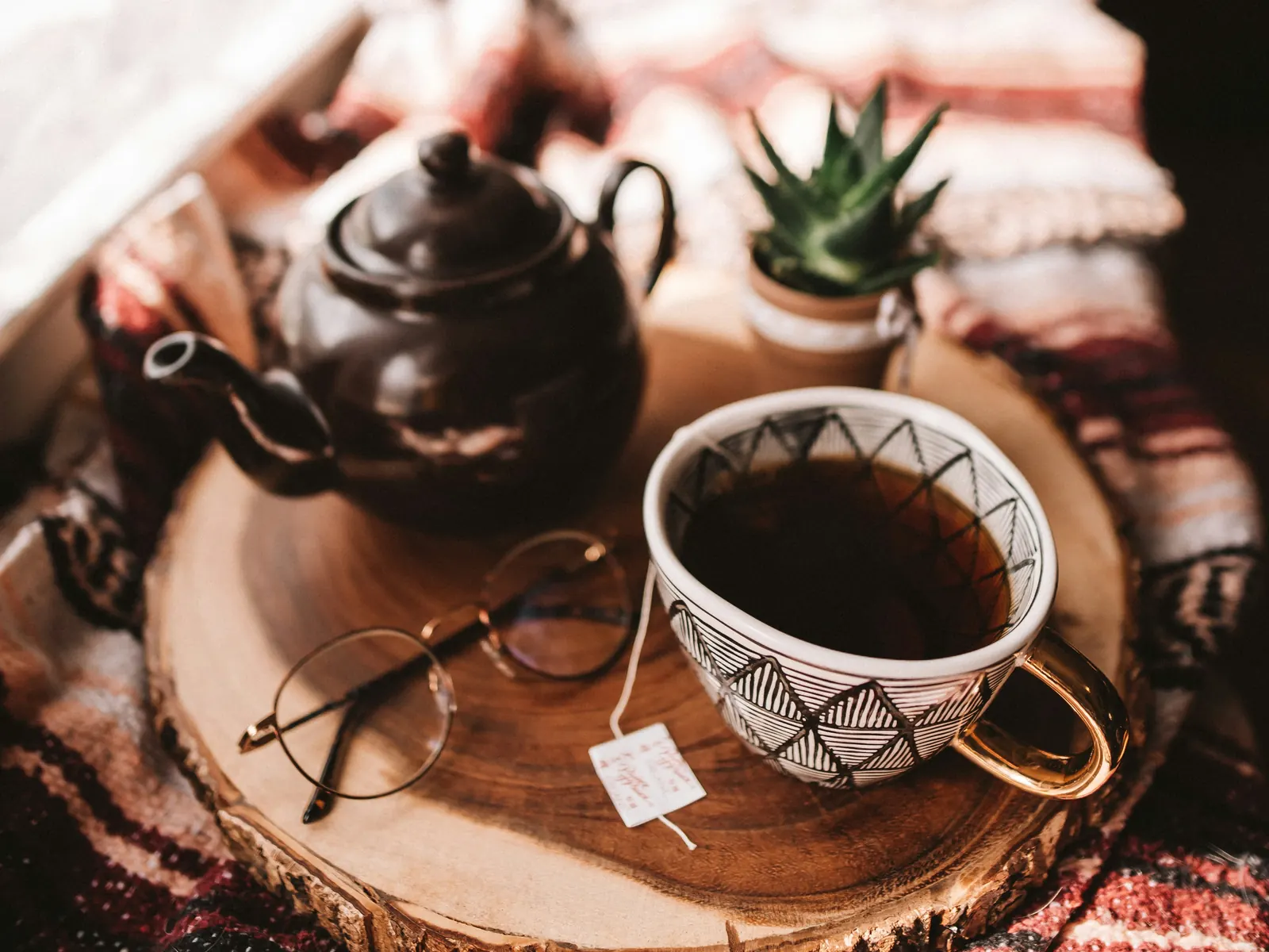 A dark lidded teapot and patterned ceramic cup on a wooden tray